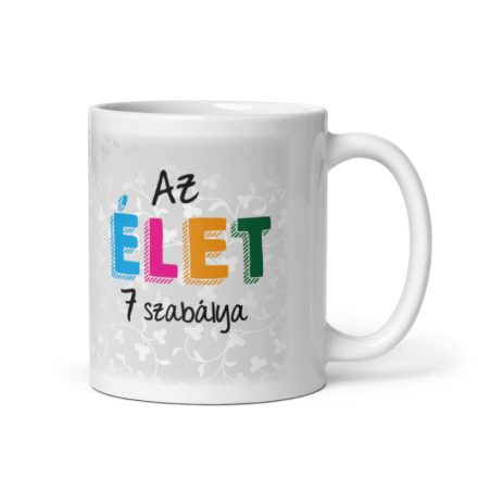 Az élet 7 szabálya feliratú fehér kerámia bögre színes ÉLET betűkkel és elegáns halványszürke indás-virágos háttérrel.