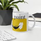 Sárga sávos paint feliratú fehér kerámia bögre fekete festőecset és fehér texturált festékfolt grafikájával.
